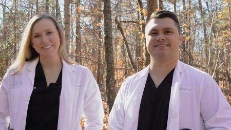 Cy and Kandis Fogleman wearing lab coats and black shirts in front of bare trees.